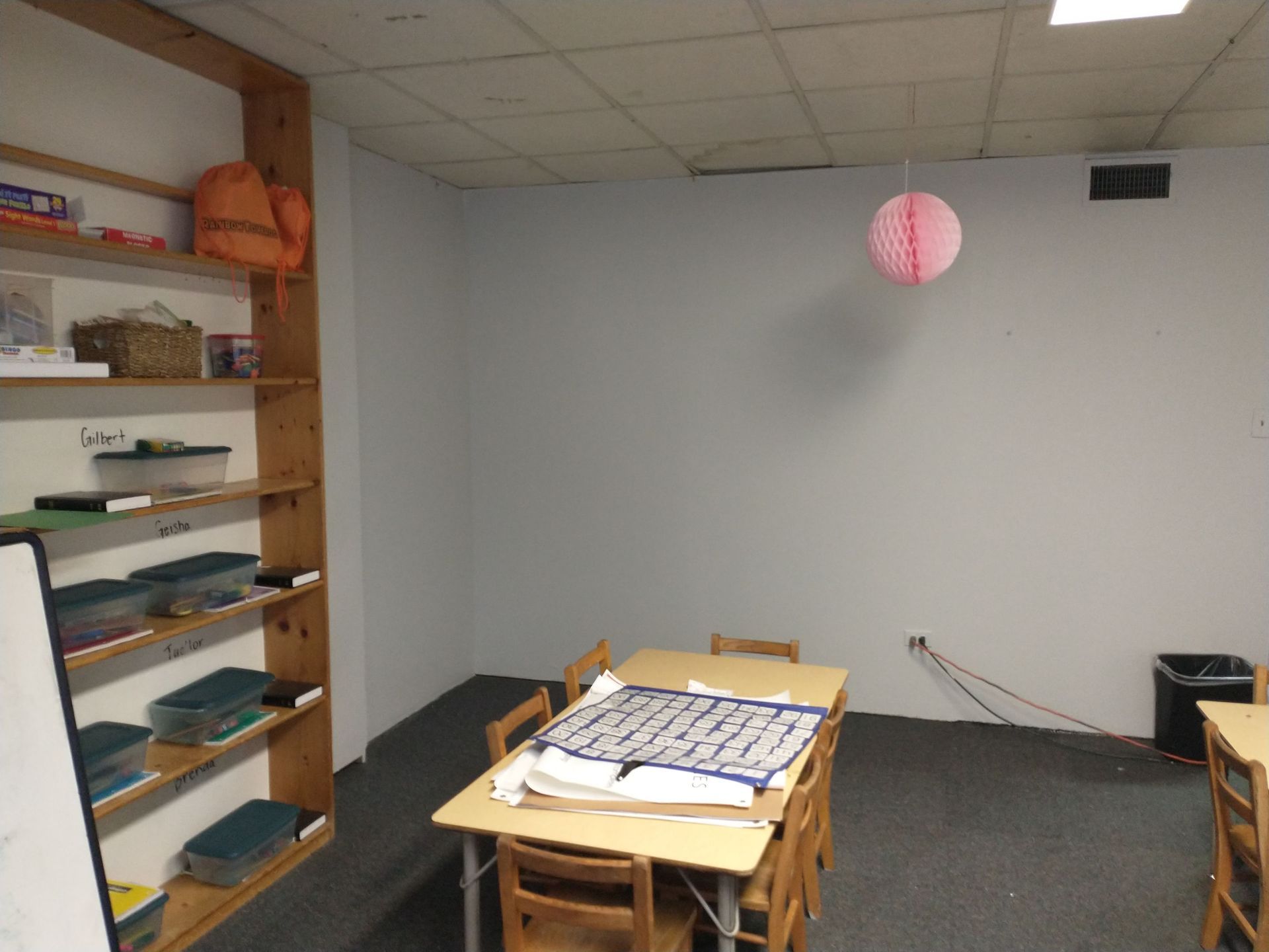 A room with a table and chairs and a pink ball hanging from the ceiling