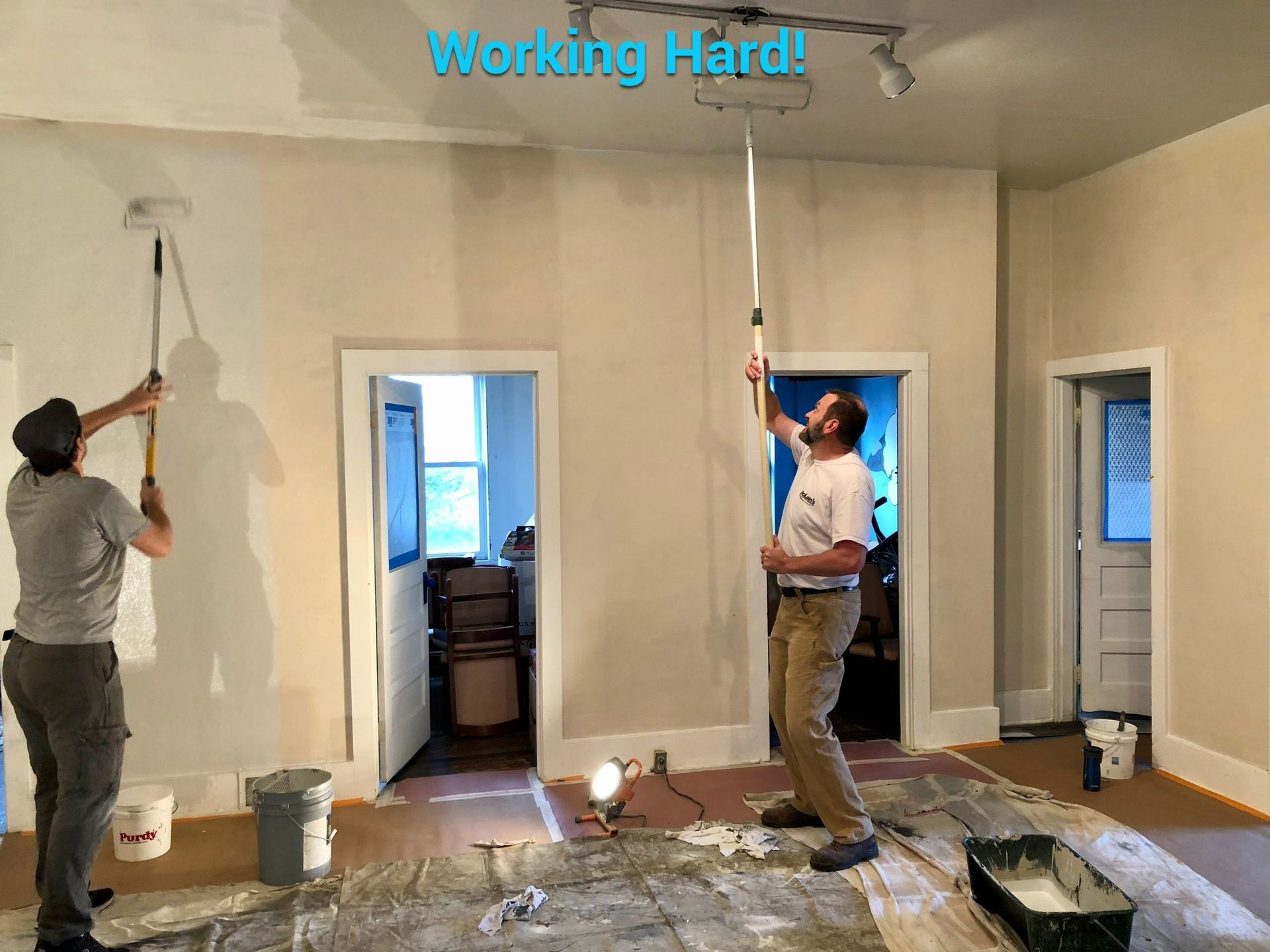 Two men are painting a wall in a room.