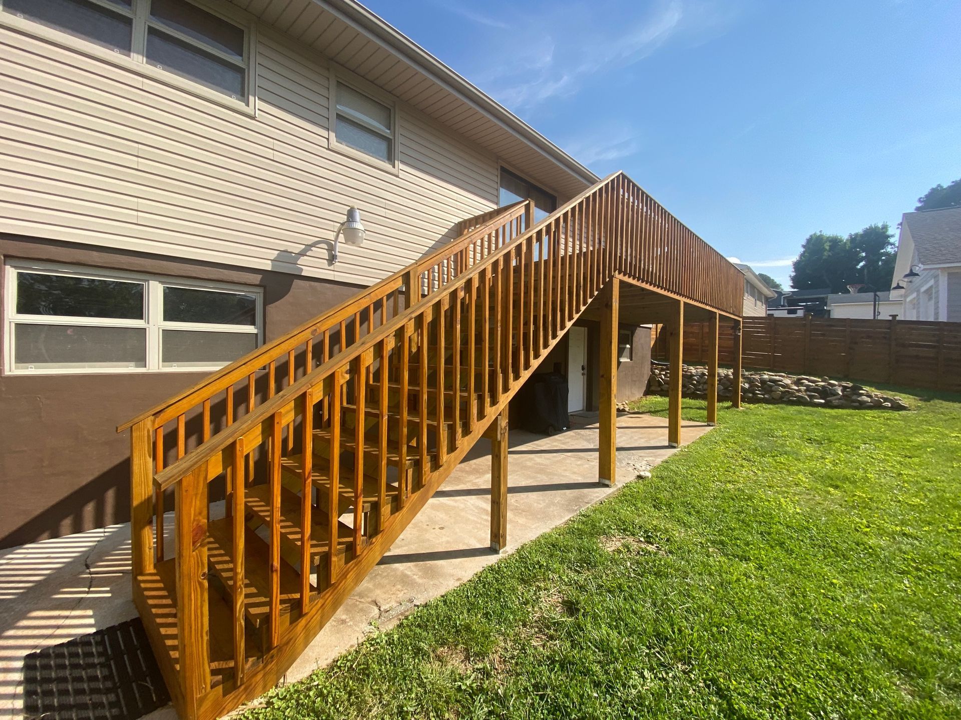 A wooden deck with stairs leading up to it is in the backyard of a house.