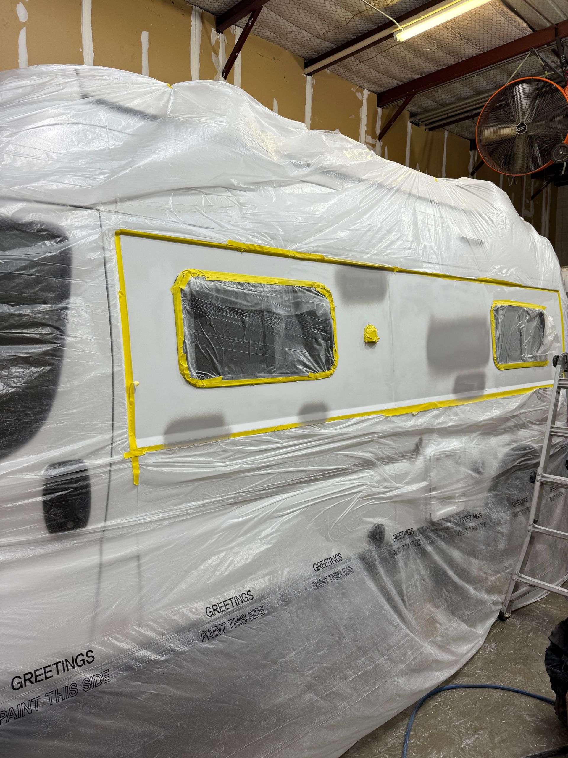 A camper is covered in plastic wrap at RV Repair Solutions being painted.