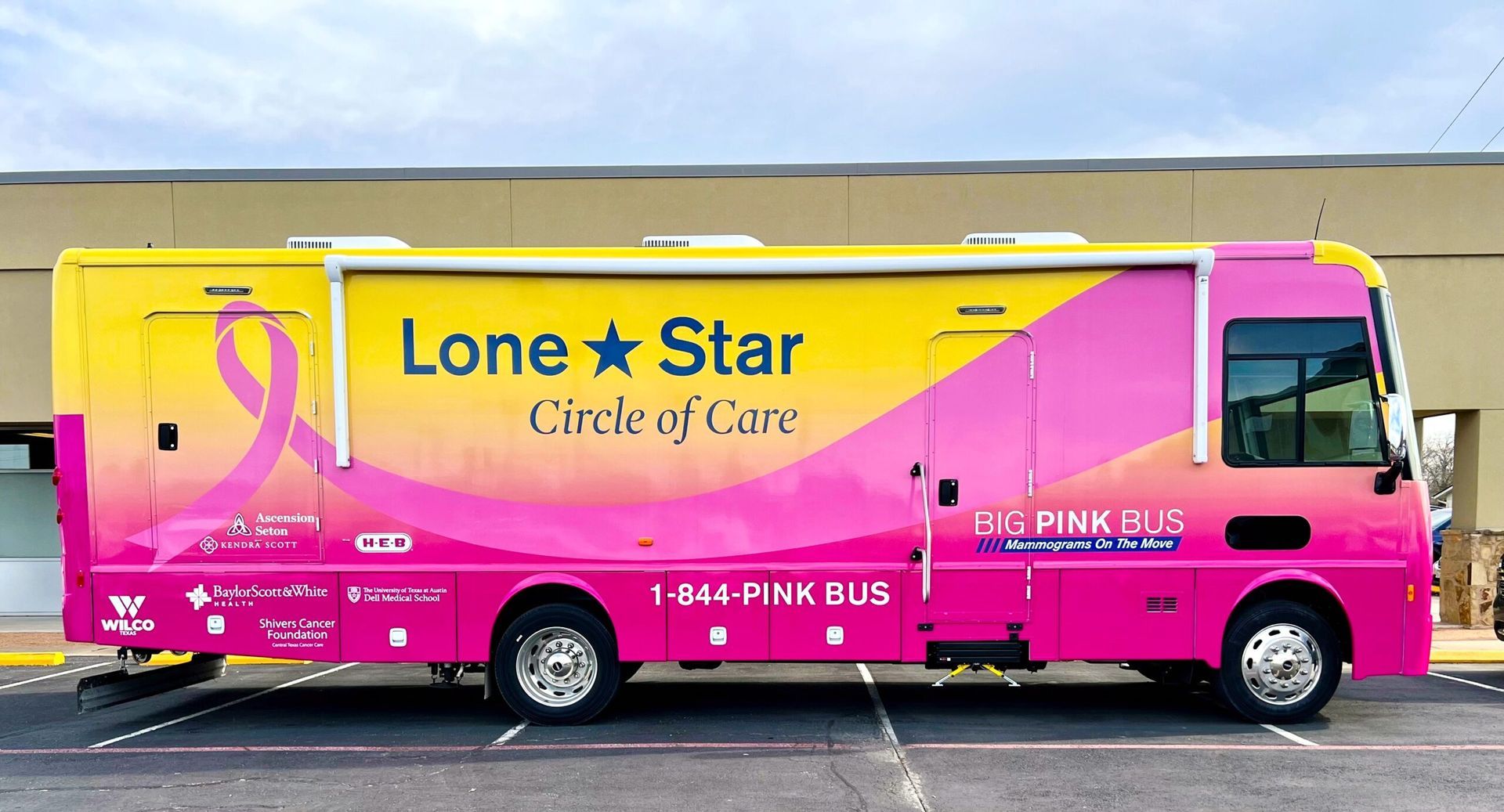 A pink and yellow lone star bus is parked in a parking lot