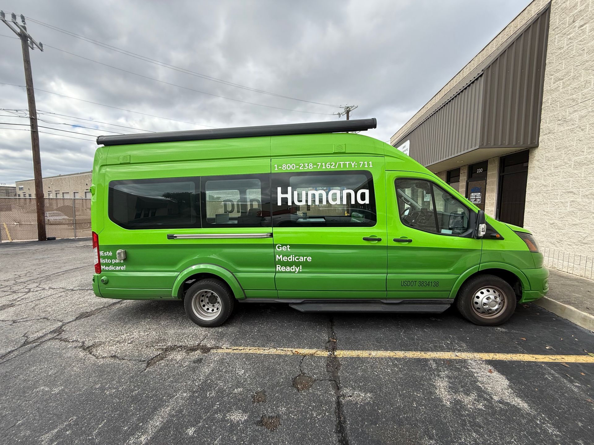 A green van is parked in a parking lot in front of a building.
