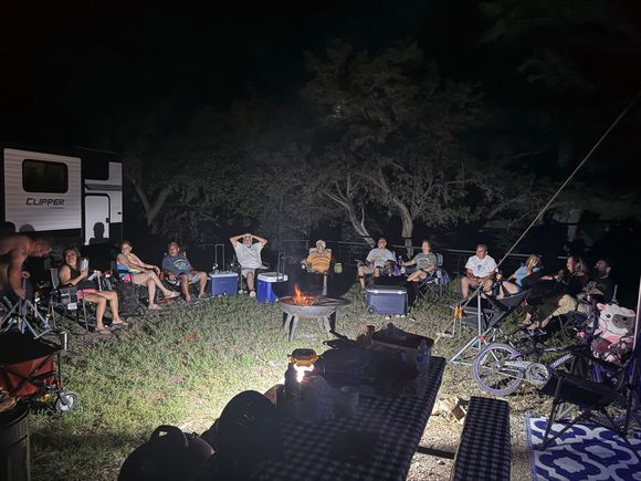 A group of people are sitting around a fire pit at night.