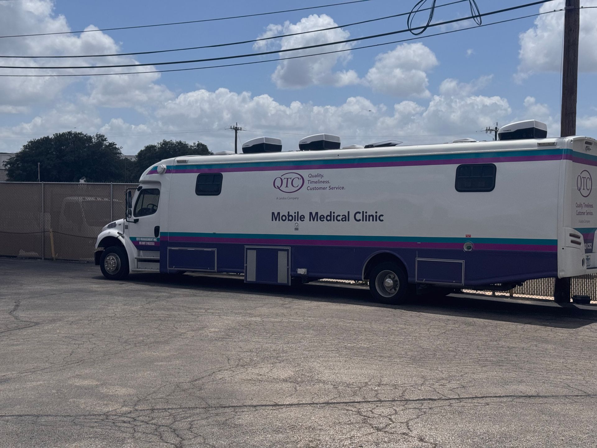 A purple and white mobile medical unit is parked in a parking lot