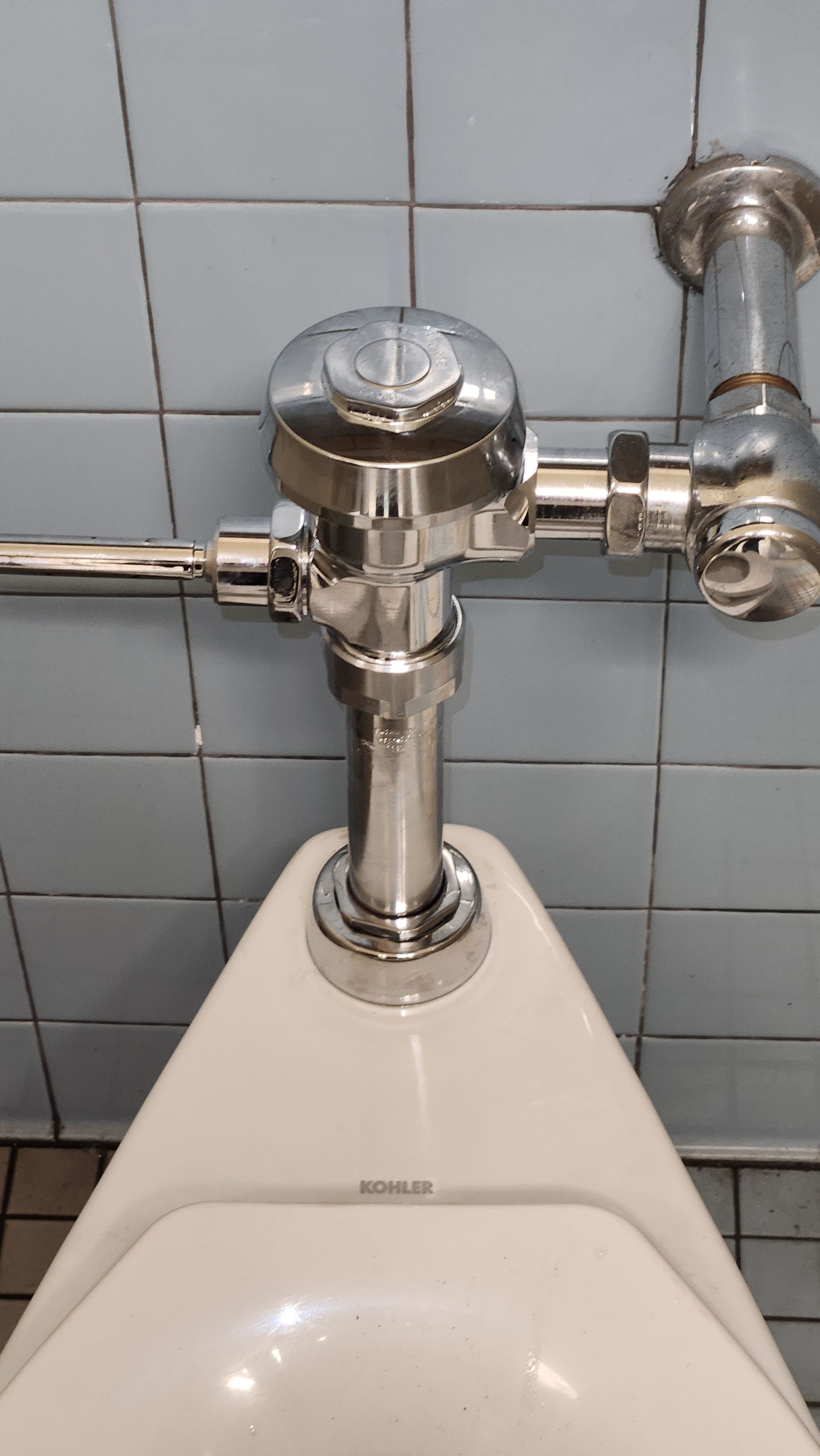 A close up of a urinal with a chrome flush valve.