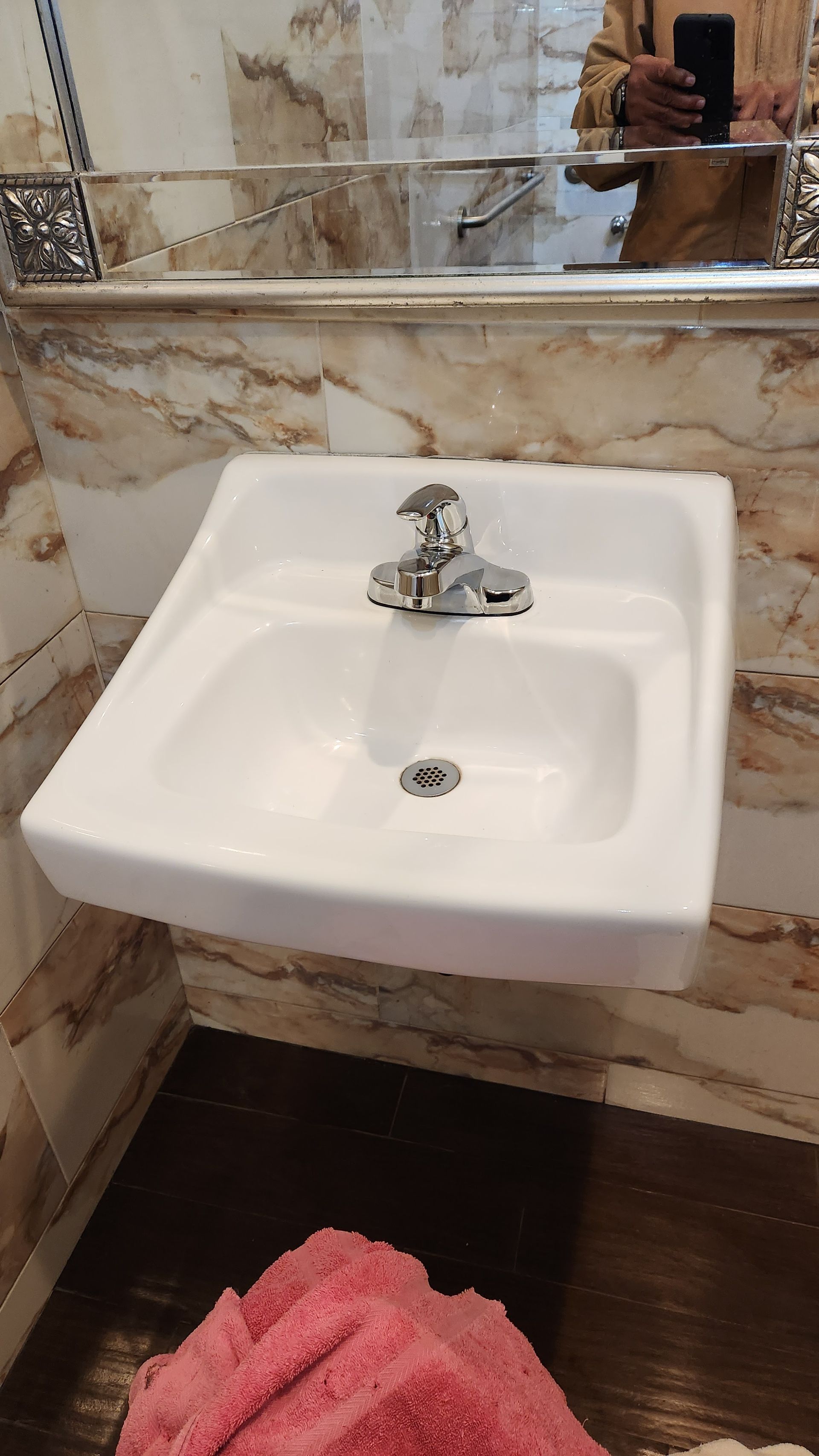 A bathroom sink with a mirror and a pink towel on the floor.