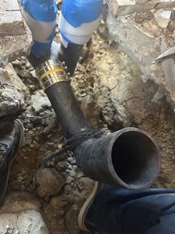 A person is working on a pipe in the dirt.