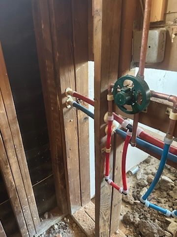 A bunch of pipes are connected to a wooden wall in a bathroom.