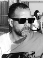 Un hombre con barba y gafas de sol lleva una camisa blanca.