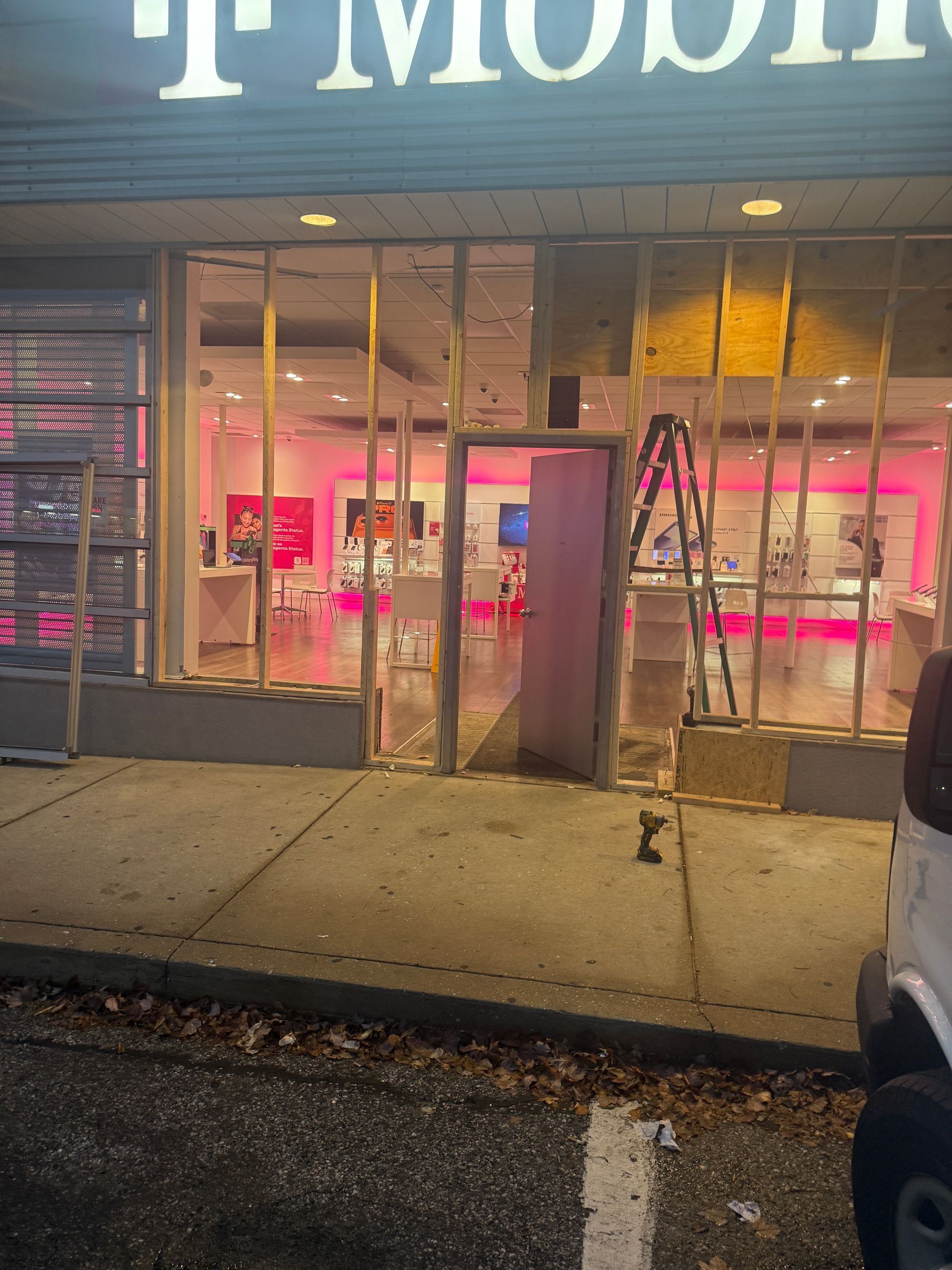 Exterior of a T-Mobile store with a shattered window, showing the inside. Construction materials are present.