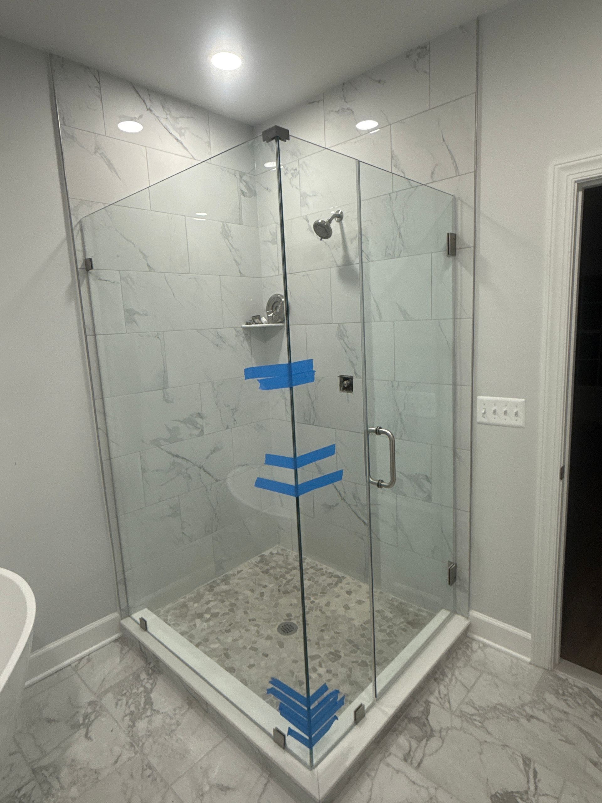 Newly installed glass shower enclosure with gray marble-look tile, corner entry.