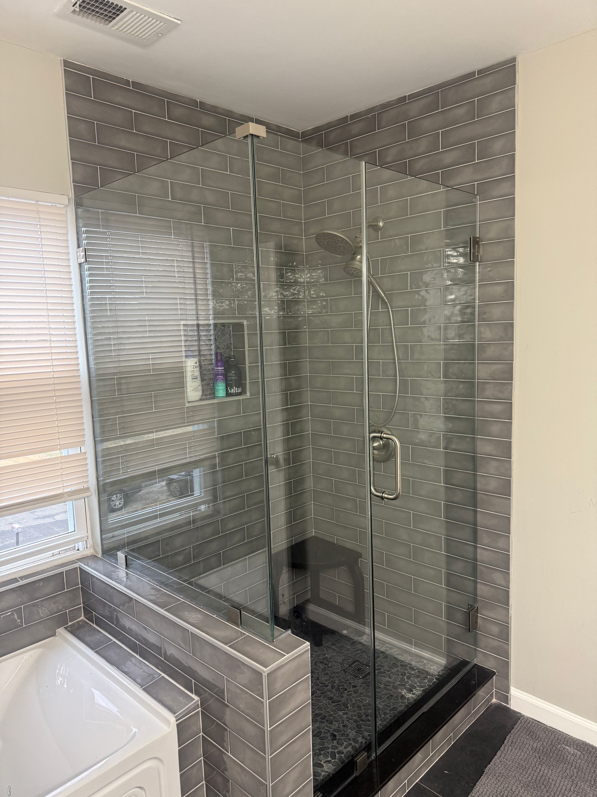 Corner glass shower with gray tiled walls and a bench.