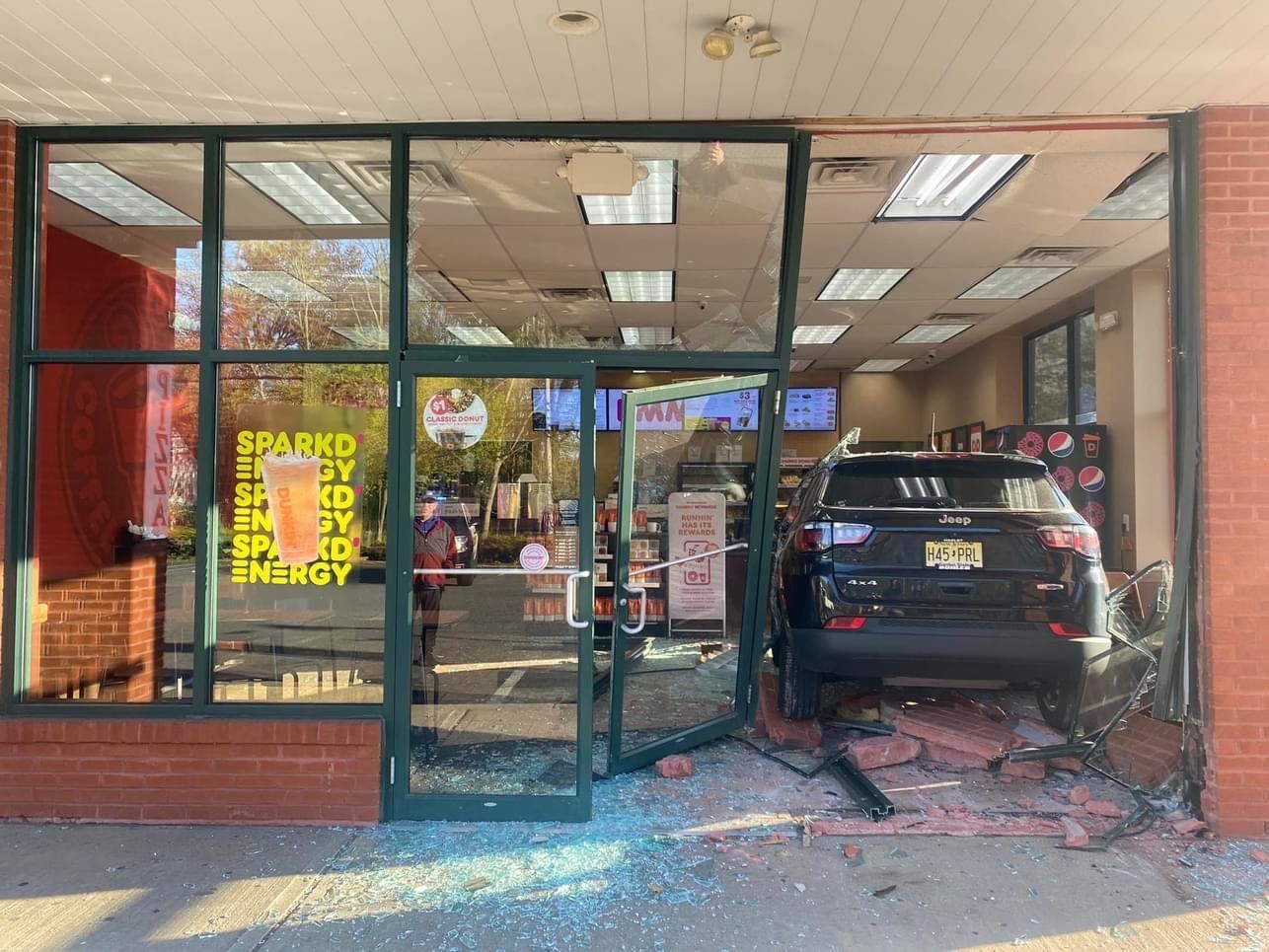 Car crashed into a store, front windows shattered. Debris and vehicle inside. Store exterior visible.