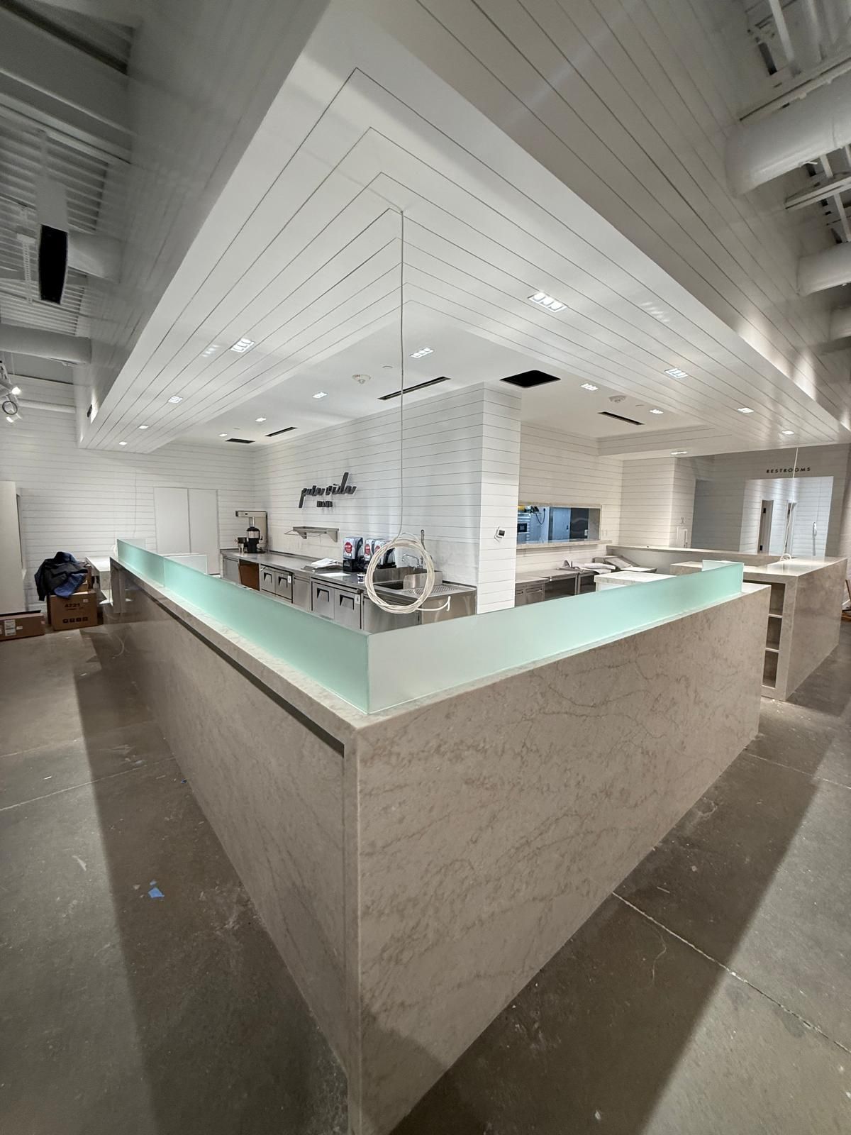A modern restaurant bar with a white textured exterior, glass countertop, and white ceiling with recessed lighting.