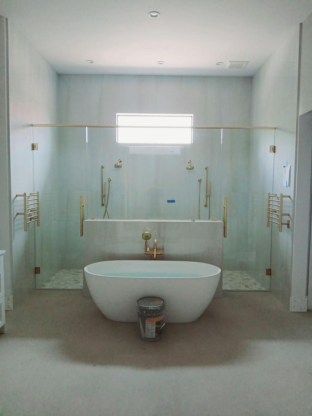 Spacious bathroom with a freestanding bathtub between two glass shower enclosures; gold fixtures.