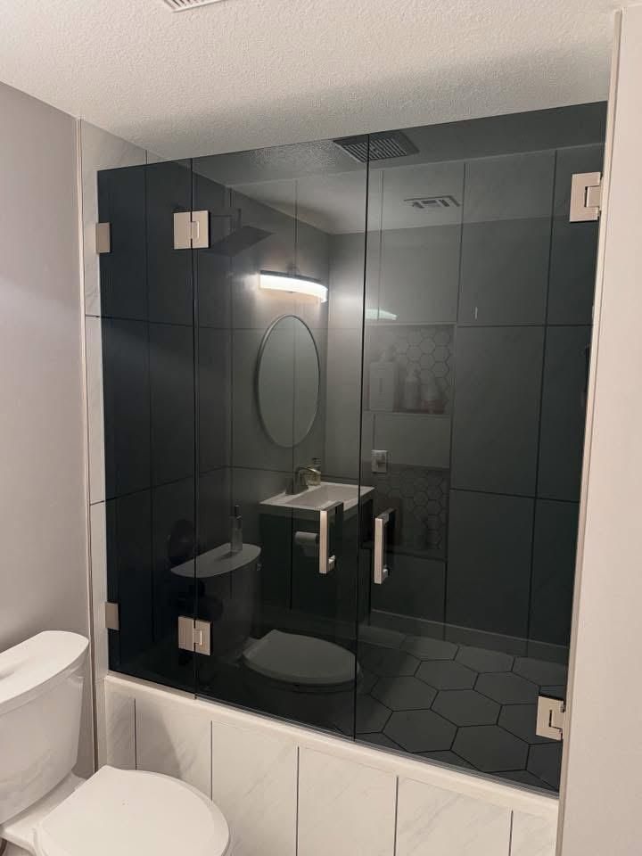 Bathroom with black glass shower enclosure, white sink, and toilet. Silver hardware.