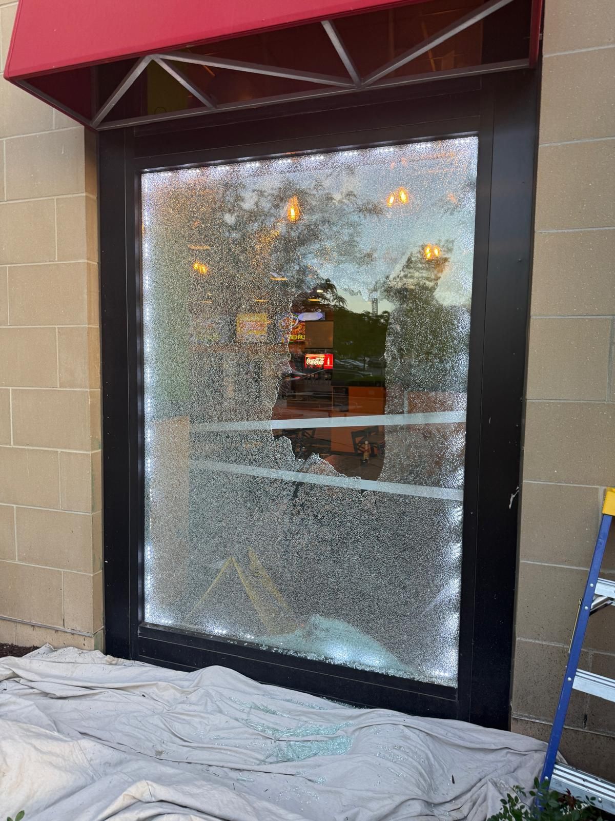 A broken window, covered in shattered glass, in a black door frame under a red awning.