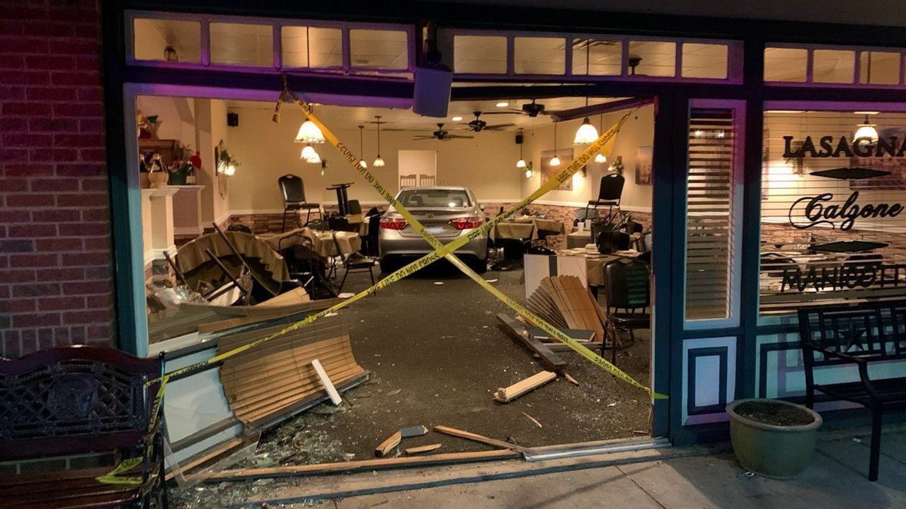 Car crashed into a restaurant; storefront damage, yellow caution tape, interior visible.