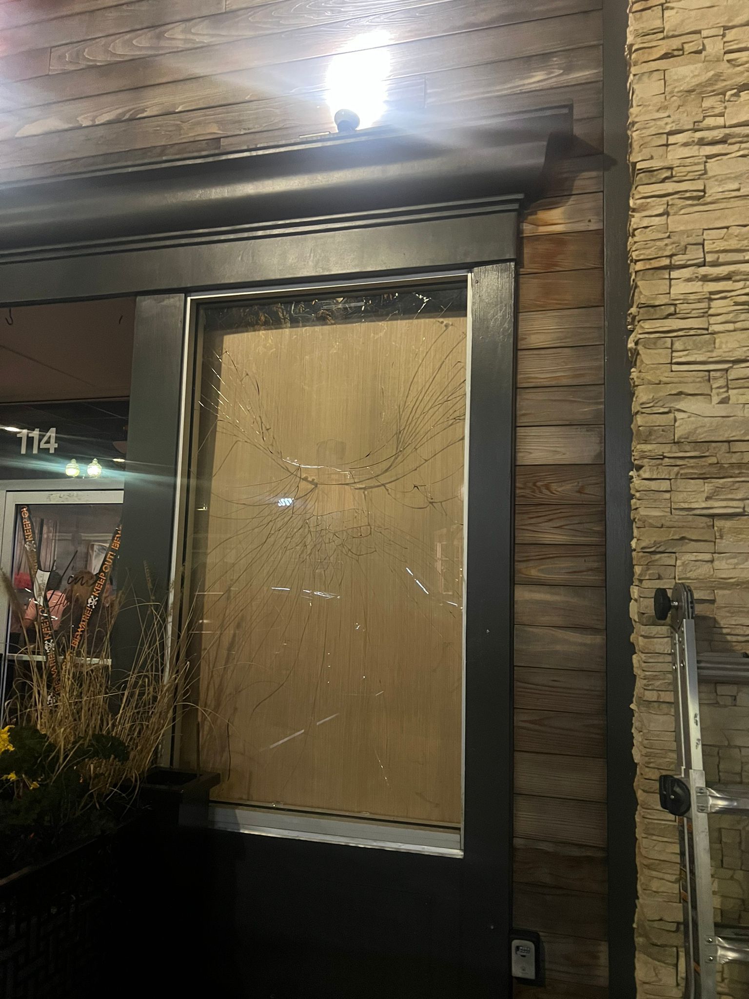 Boarded-up storefront window with a wooden panel, beside a stone-textured wall.