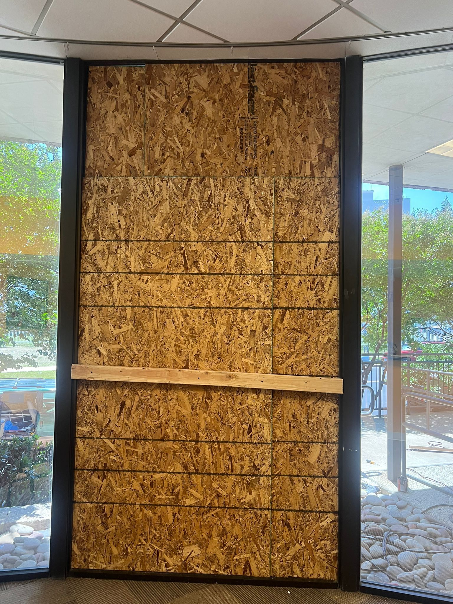 Wall blocked with wood panels in a window frame, covering glass. Outside, blurred foliage.