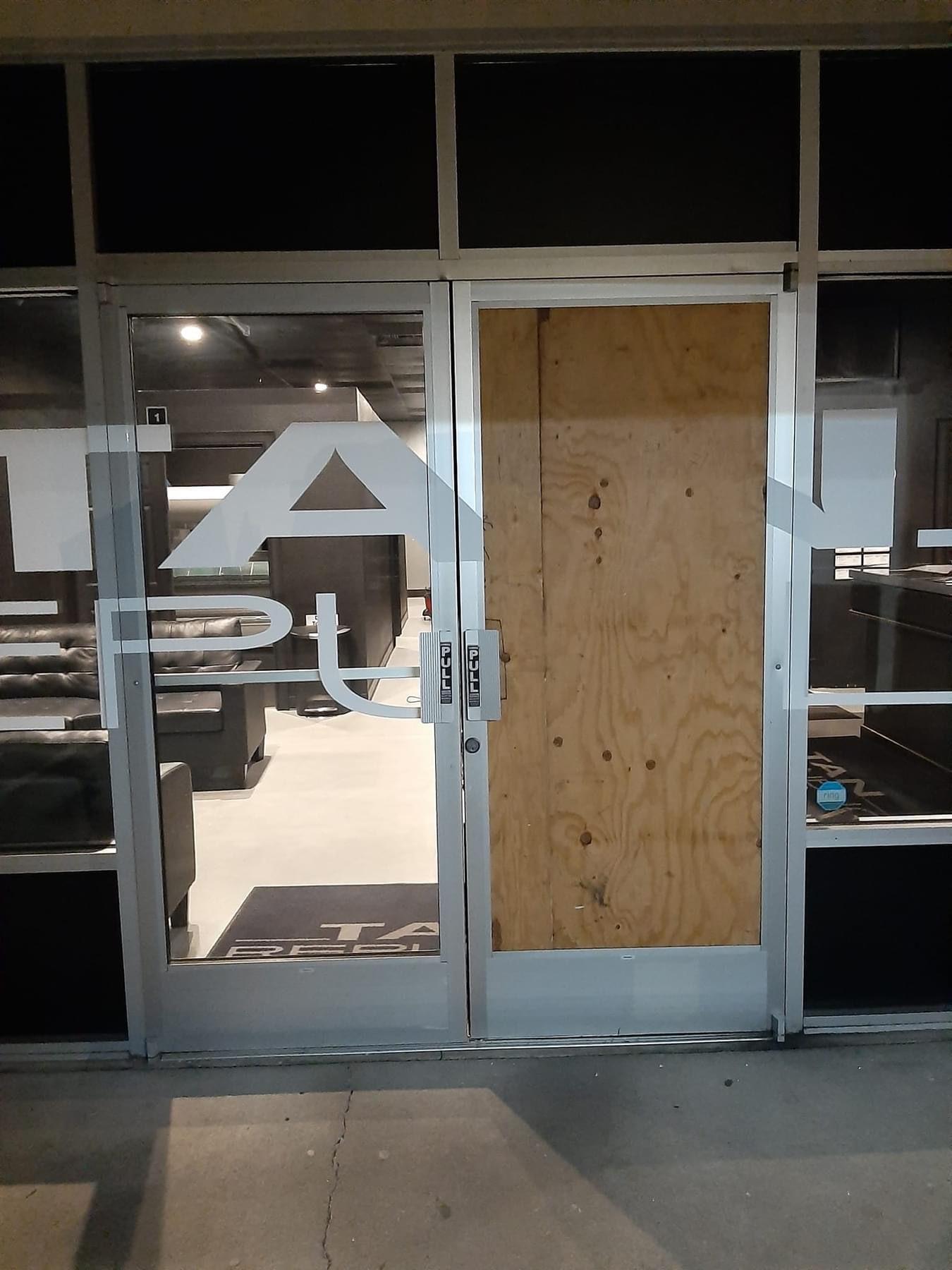 Storefront with one door boarded up, partial signage visible. Night setting, glass windows.