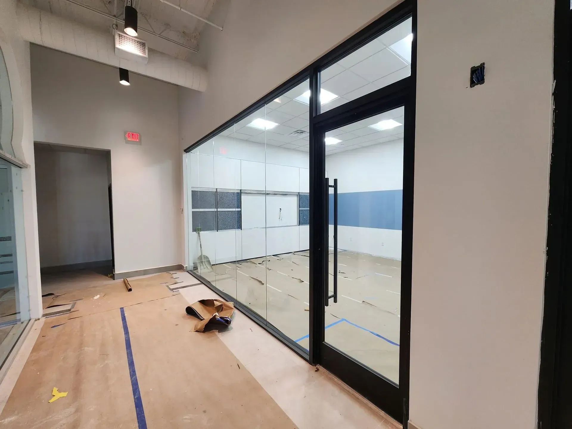 Interior of a commercial space, showing a glass-walled office with a black door. The space has new flooring.