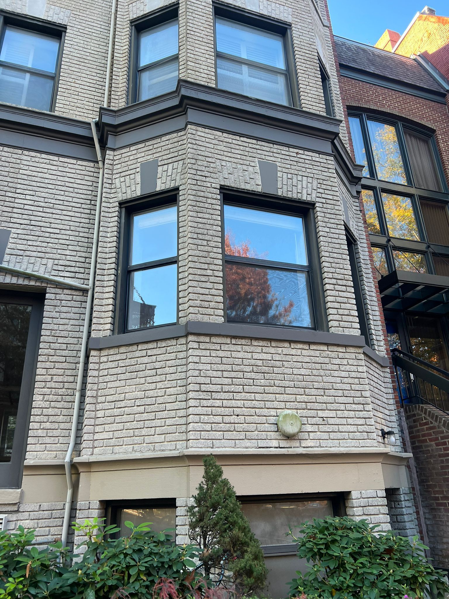 Gray brick facade of a multi-story building with dark window frames and a small garden at the base.