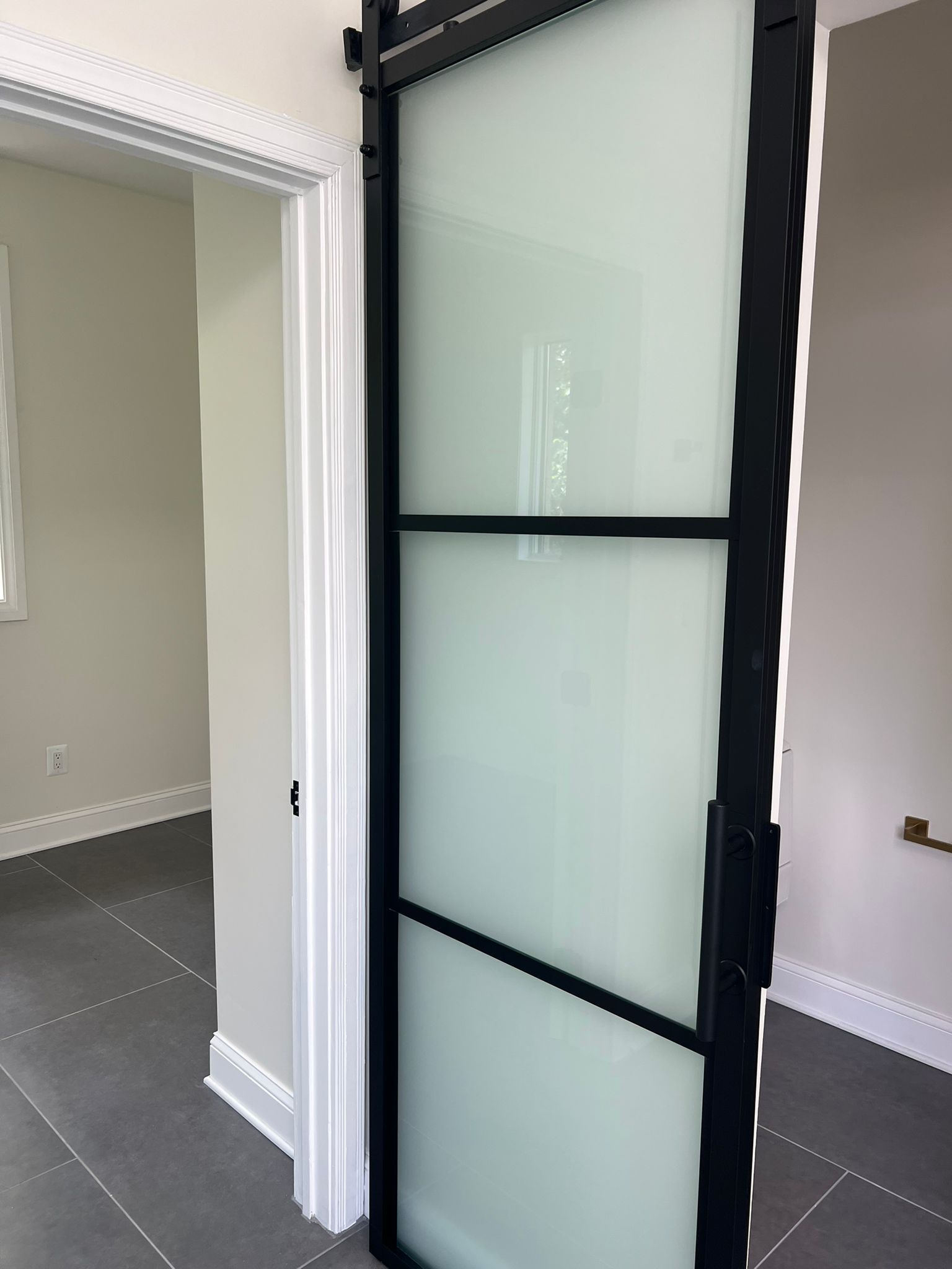 Black framed sliding glass door with frosted glass, open to a room with gray walls and flooring.