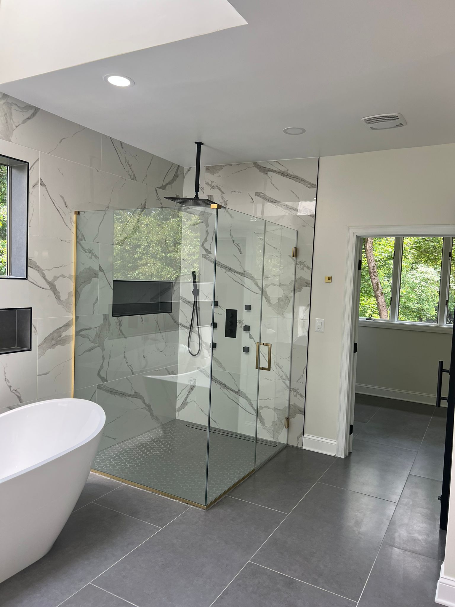 Modern bathroom with marble tile, glass shower, freestanding tub, and a doorway.