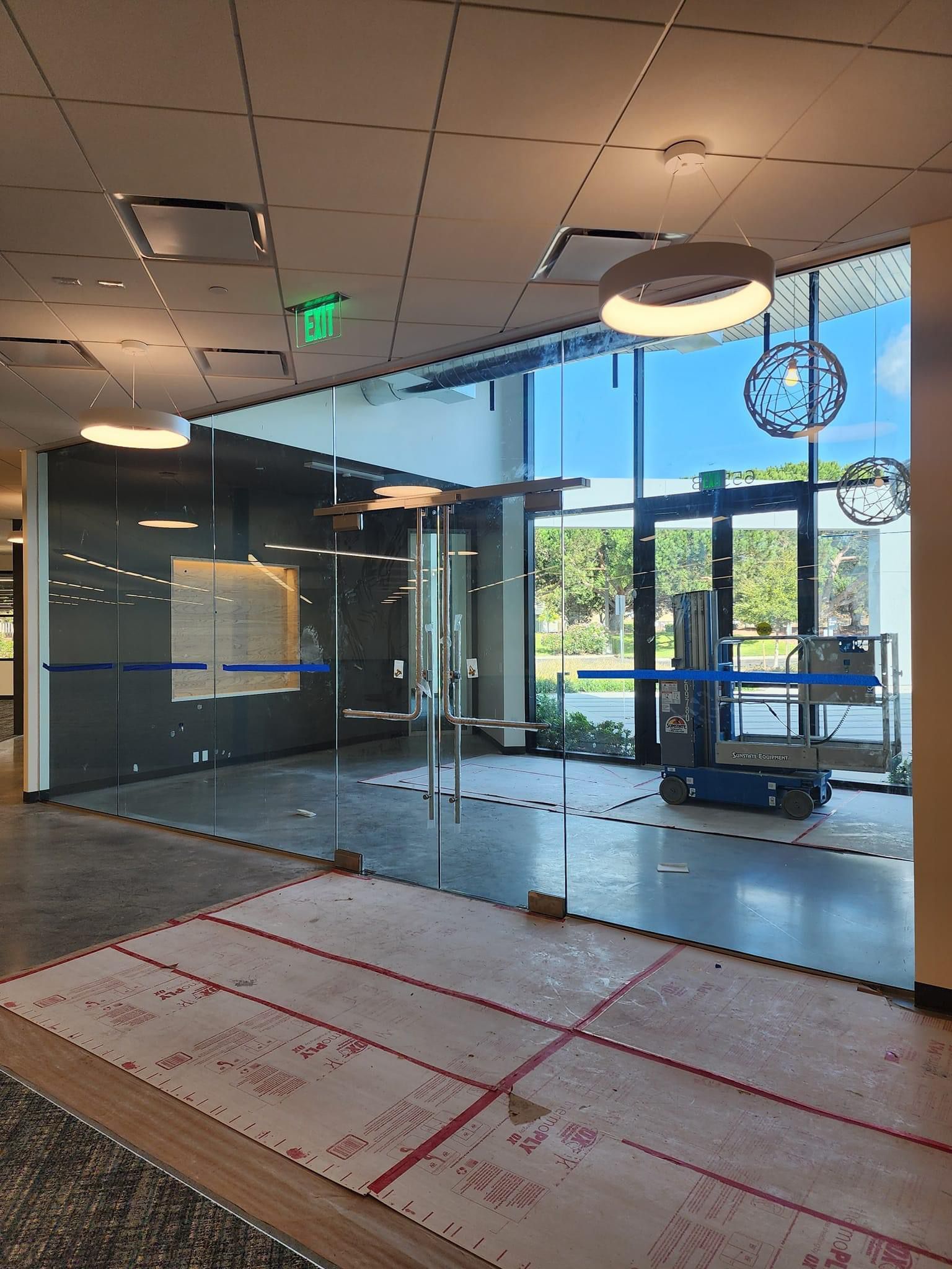 Glass office entrance with natural light, a blue scissor lift, and unfinished flooring.
