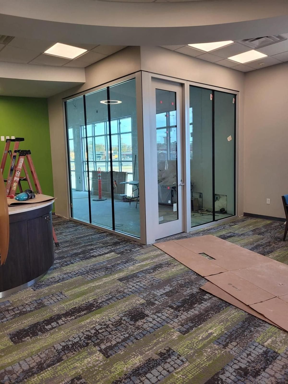 Interior with glass-walled room, door, and unfinished walls, next to green and gray accents.