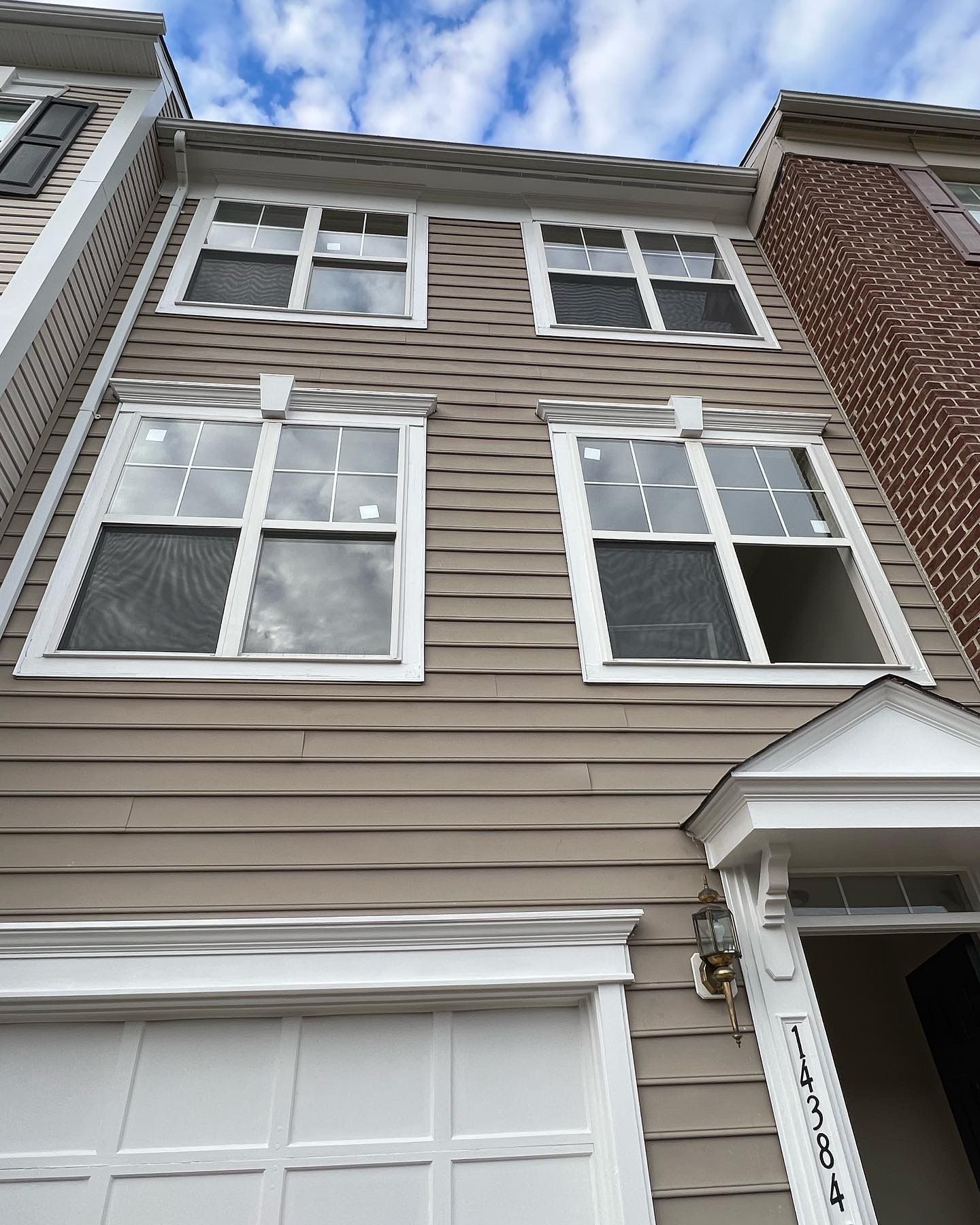 Tan townhome exterior with four windows. White trim, garage door, and blue sky.