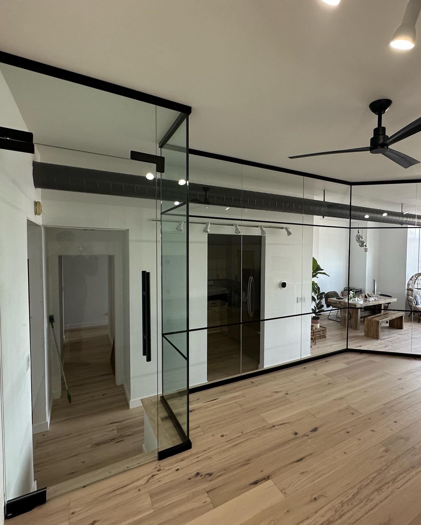 Modern interior with glass walls and black frames. Light wood floors, white walls, and a ceiling fan are also visible.