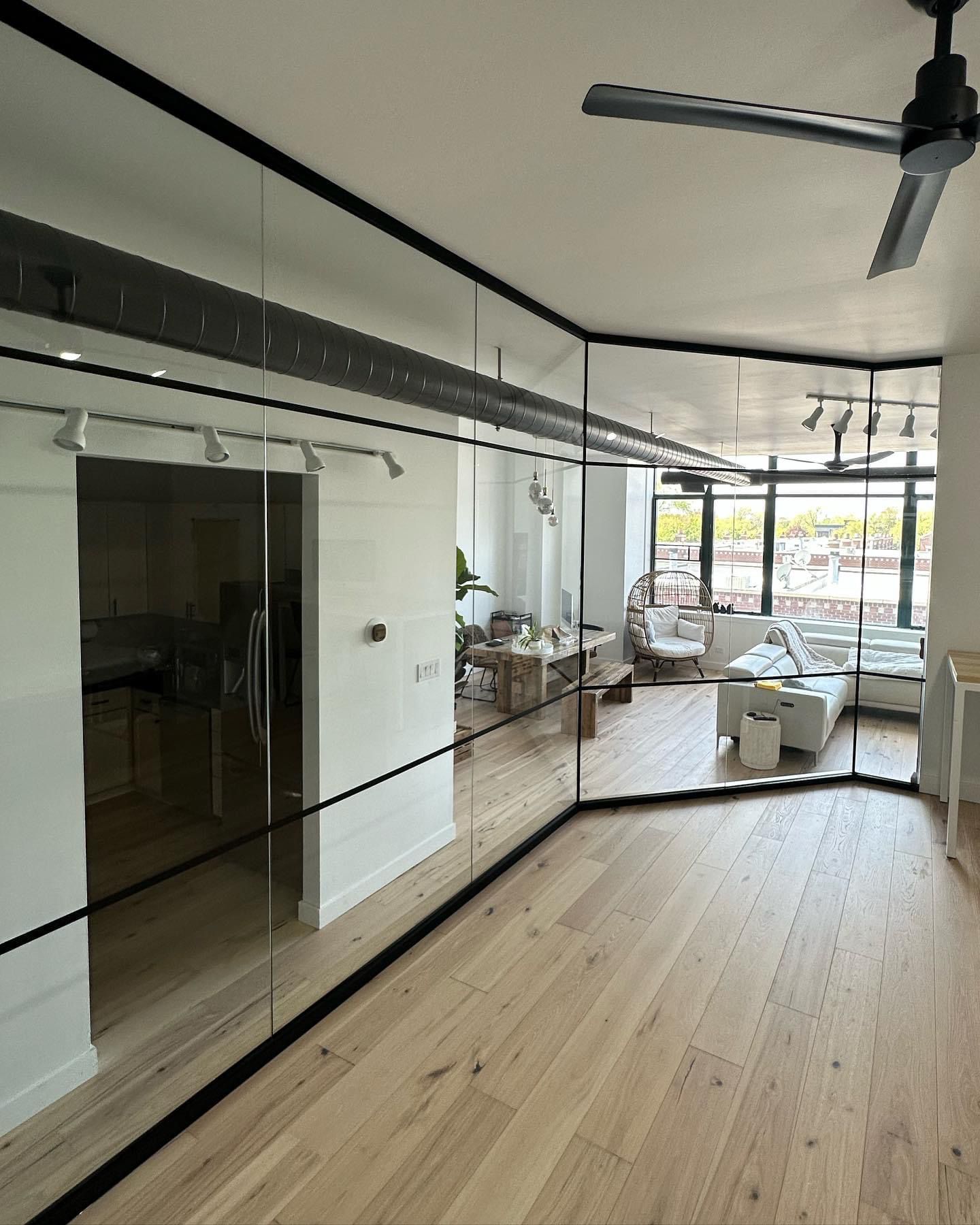 Modern interior with mirrored walls and light wood floors. Sunlight streams through large windows.