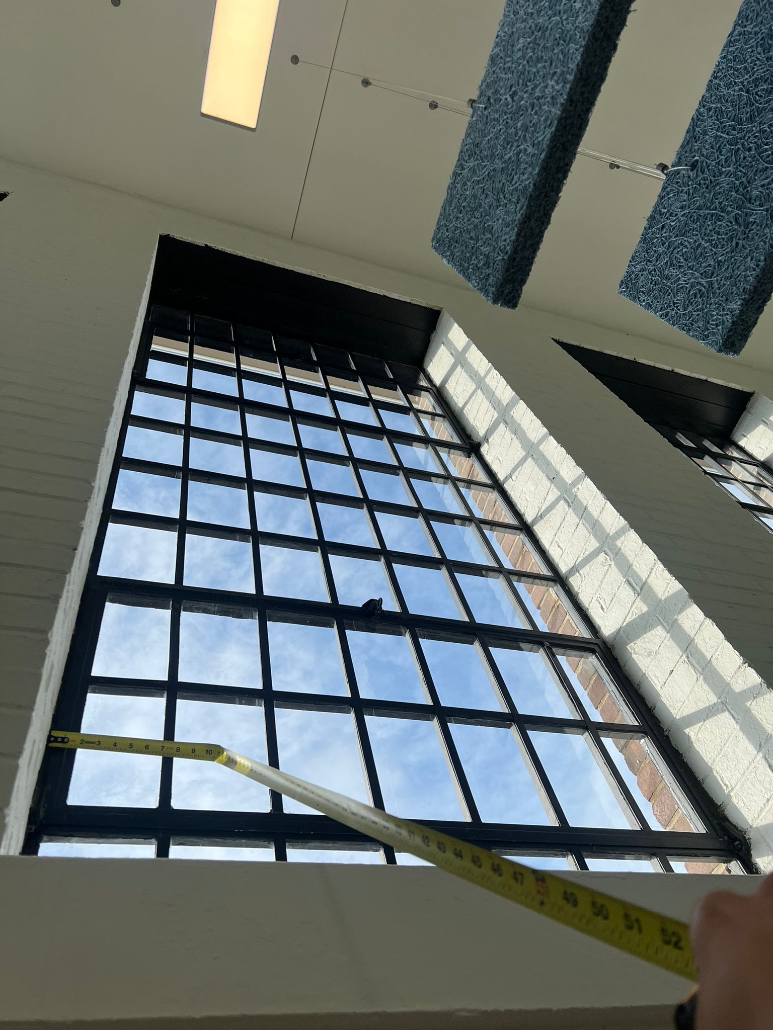 Large window with black grid, tape measure extended. Blue sky visible through the glass.