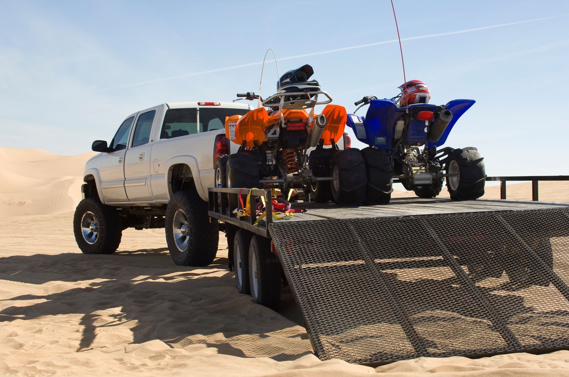 View of a custom-built trailer attached to a grey truck with two four-wheelers on top. 