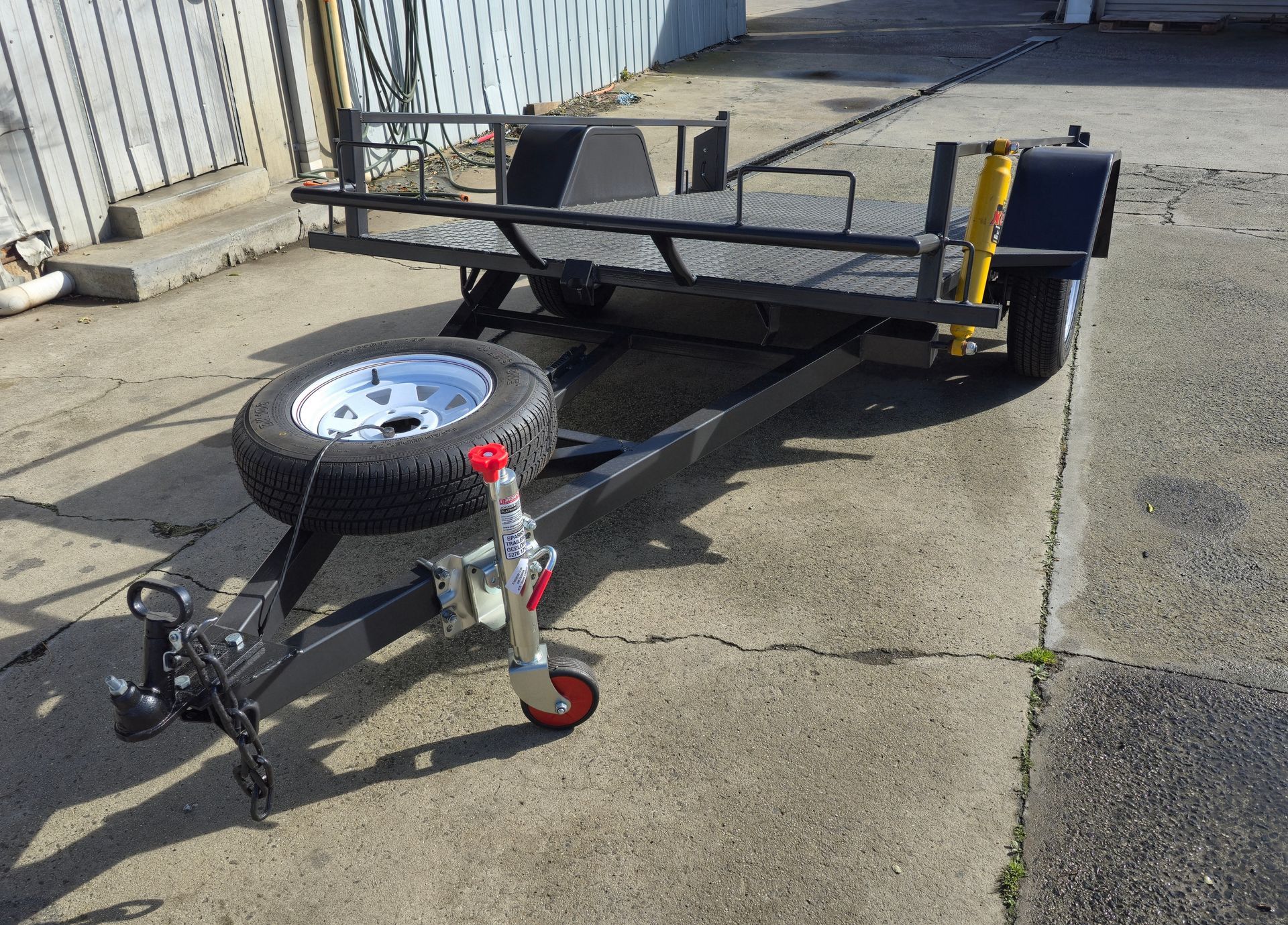 Black utility trailer with spare tire, on a concrete surface.