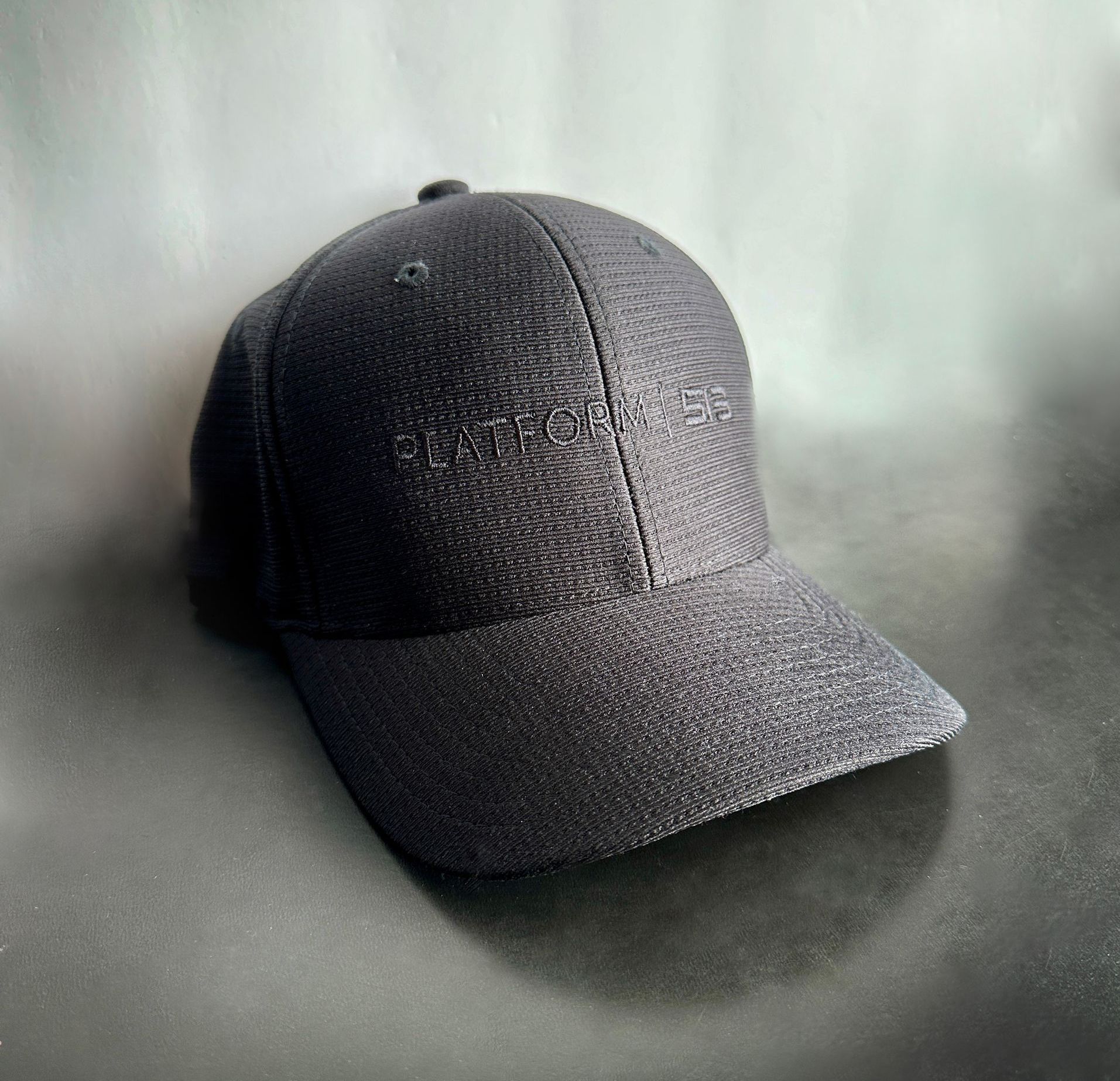 A black baseball cap is sitting on a black surface.