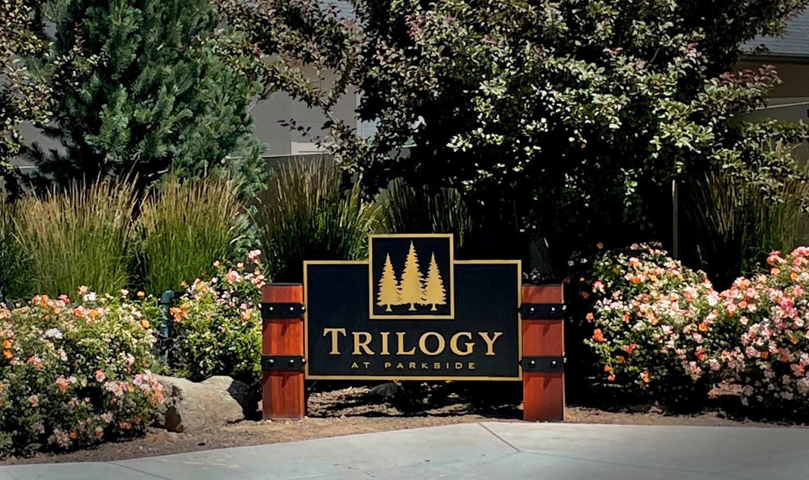 A trilogy sign is surrounded by bushes and trees