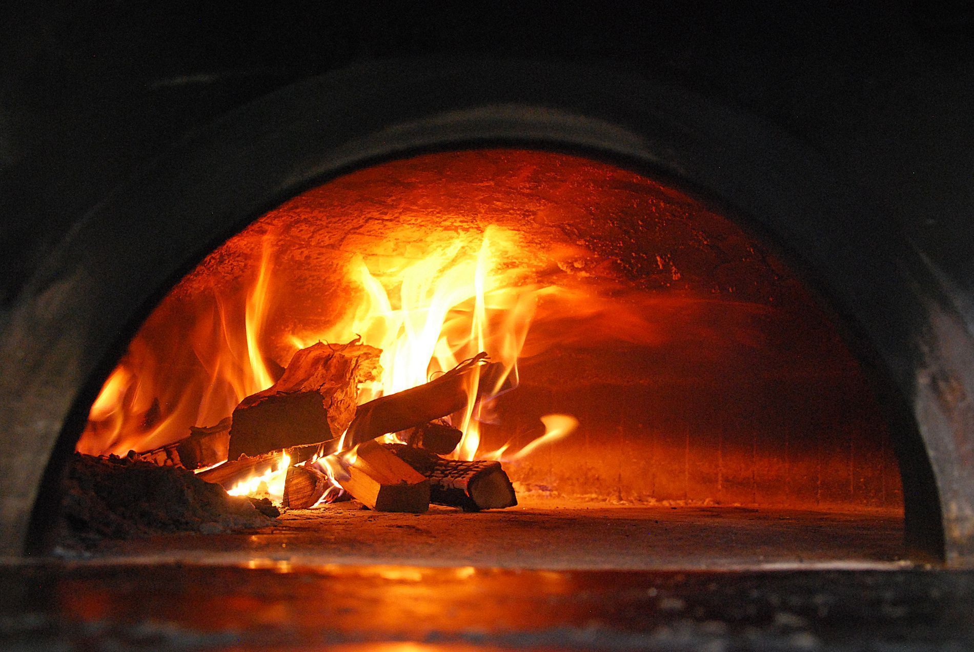 Fiamme arancioni brillanti ardono da una catasta di legna all'interno di un forno di pietra scuro e arcuato.