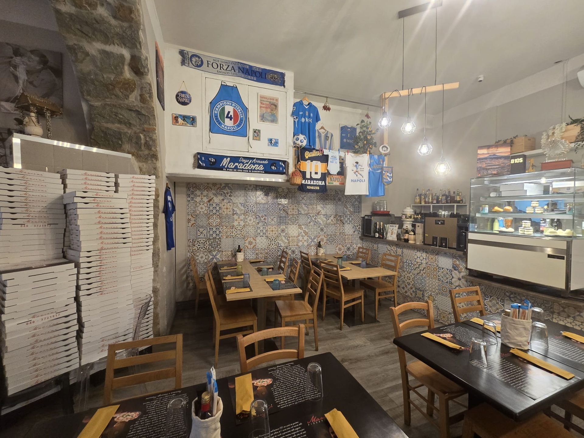 L'interno accogliente di un ristorante italiano è caratterizzato da tavoli in legno, pareti piastrellate e cimeli sportivi appesi sopra il bancone.