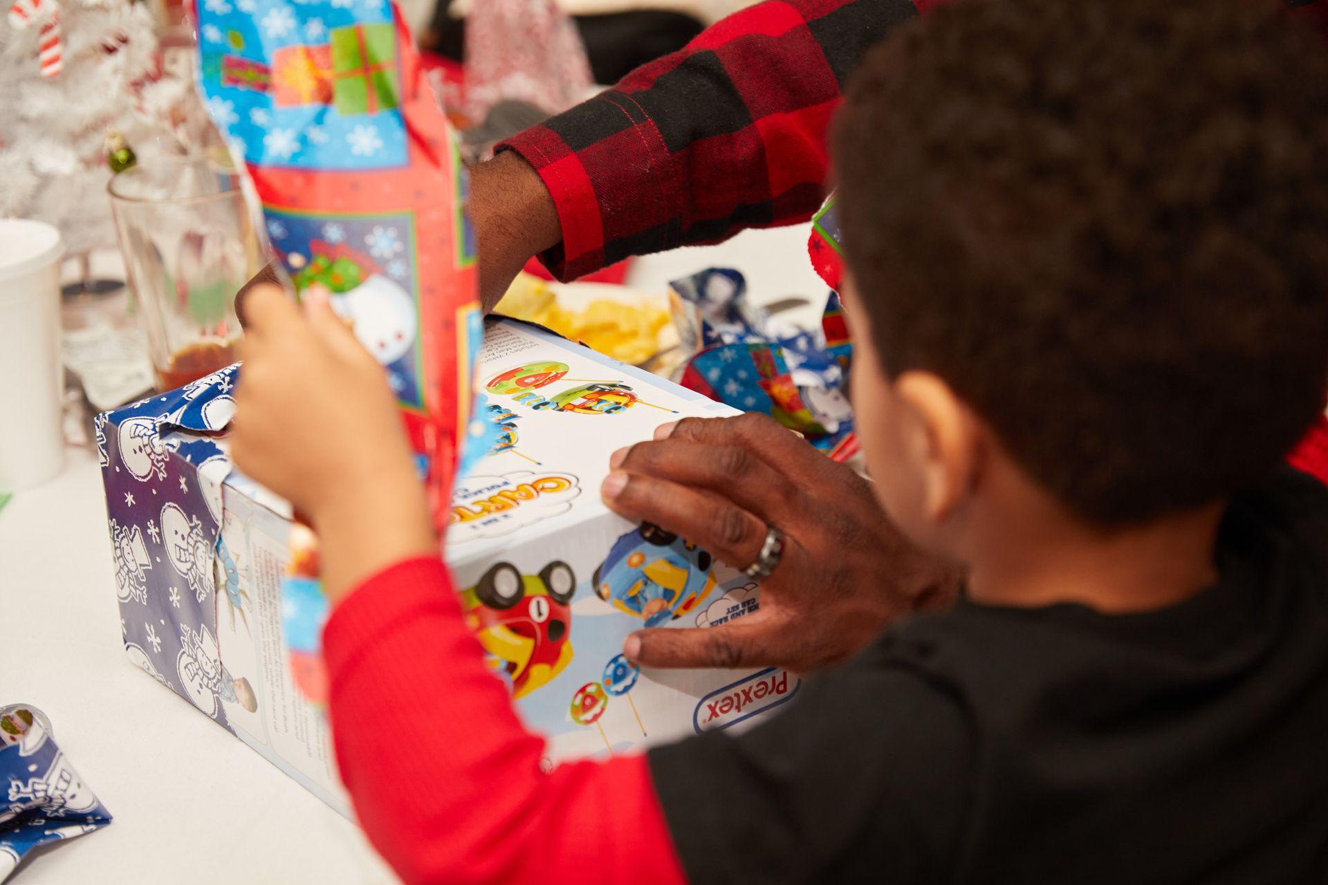A young boy is opening a christmas present while sitting at a table.