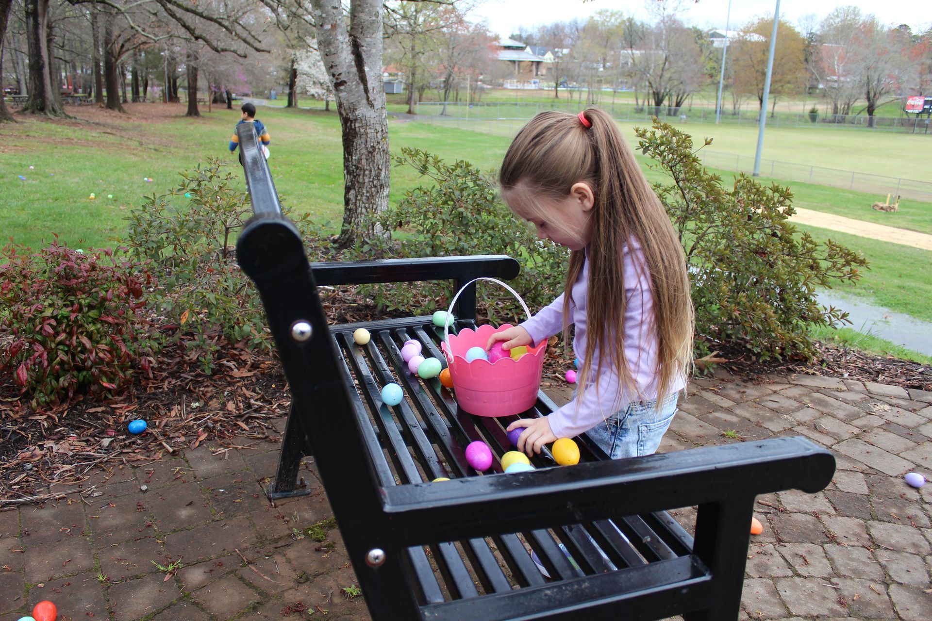 A little girl is sitting on a park bench looking at easter eggs.