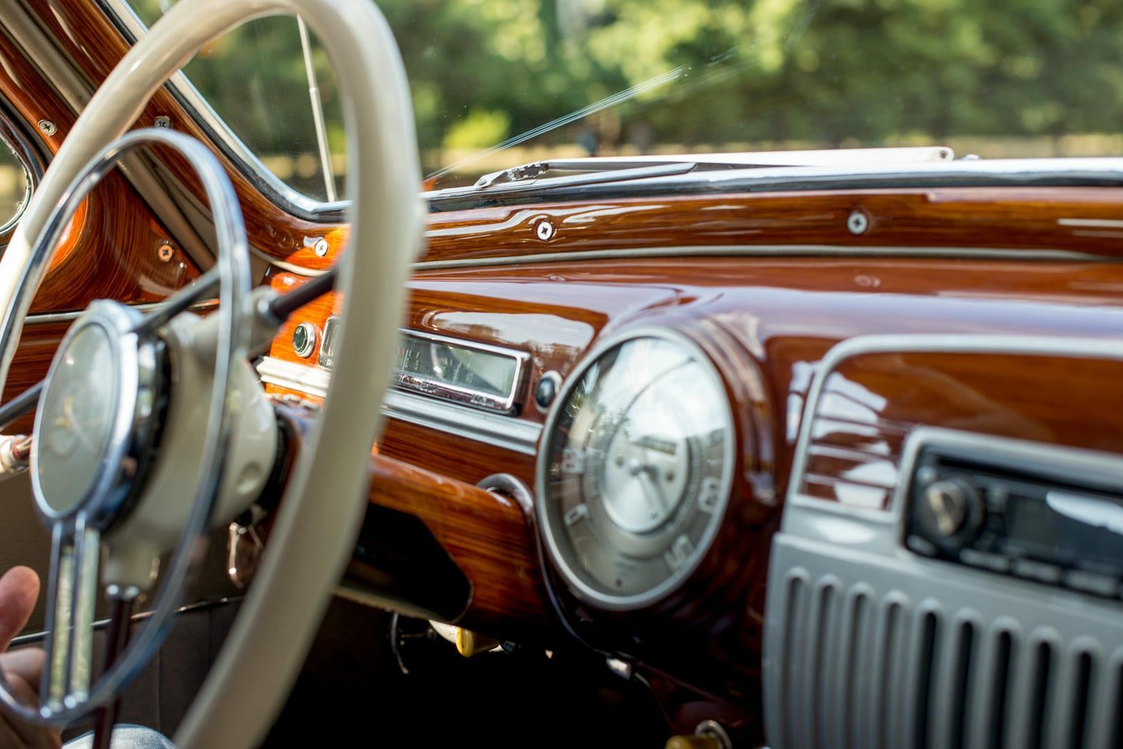 Interior of classic car with wood-grain dashboard, cream-colored steering wheel, and vintage gauges.