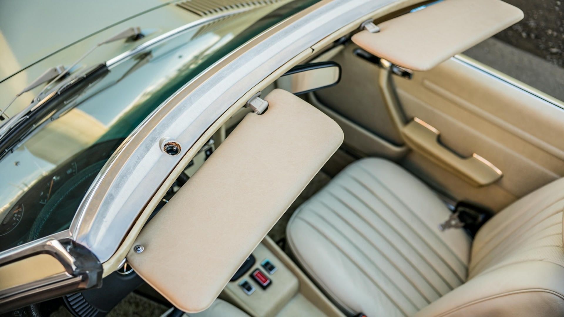 Interior of a classic car with open, cream-colored sun visors, white seats, and dashboard details.