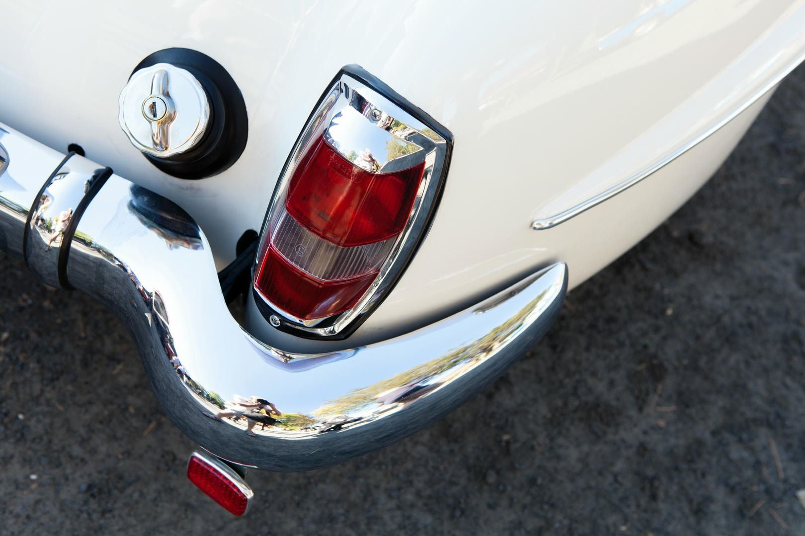 Chrome bumper, tail light, and fuel cap on a white vintage car.