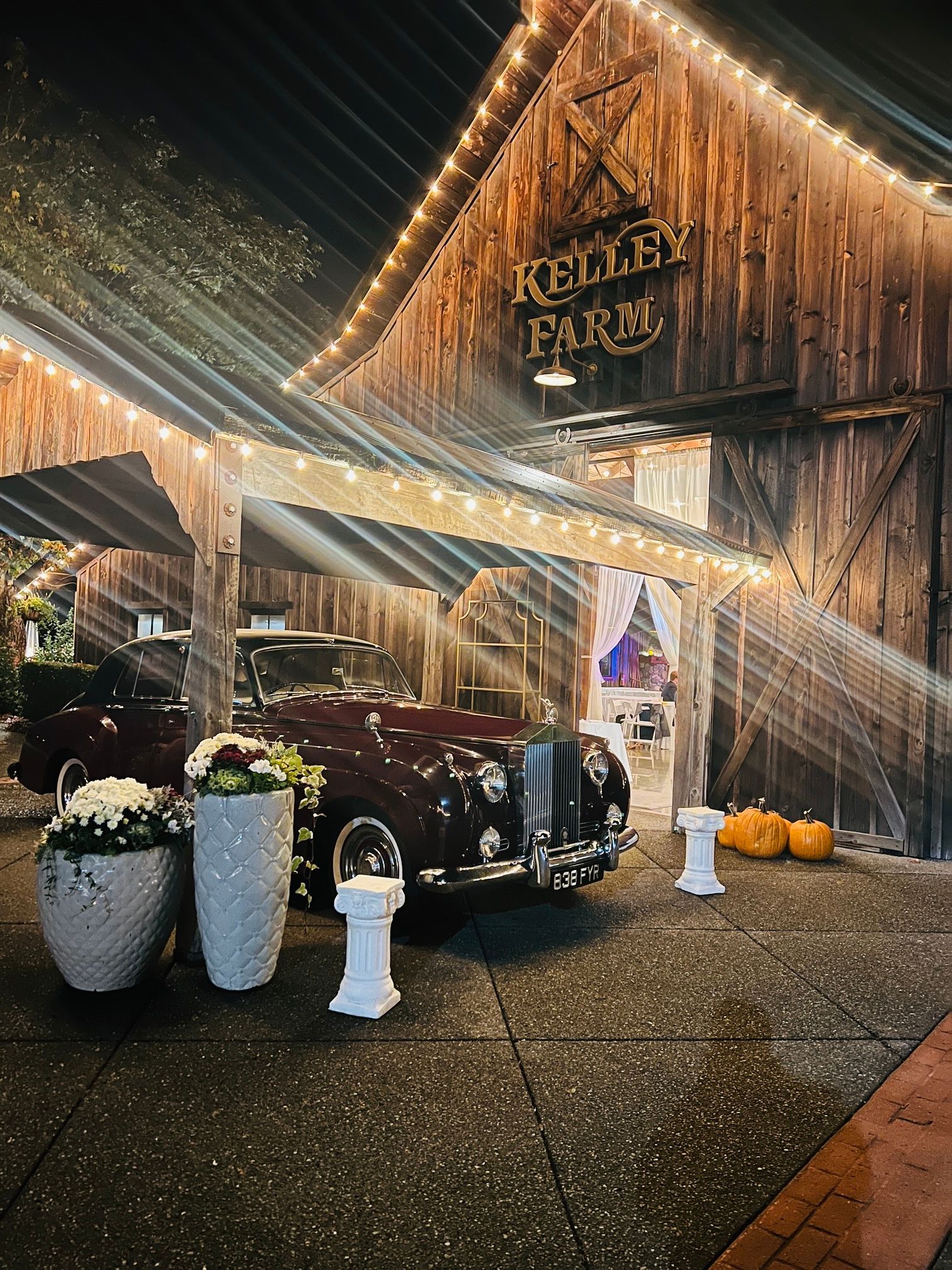 Woman with red hair exiting a turquoise vintage car in a grassy field, wearing a polka dot dress.