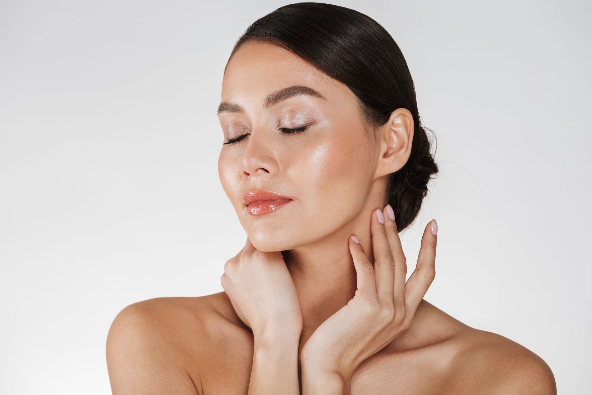 Woman with fair skin, eyes closed, touching her neck with both hands, against a light background.
