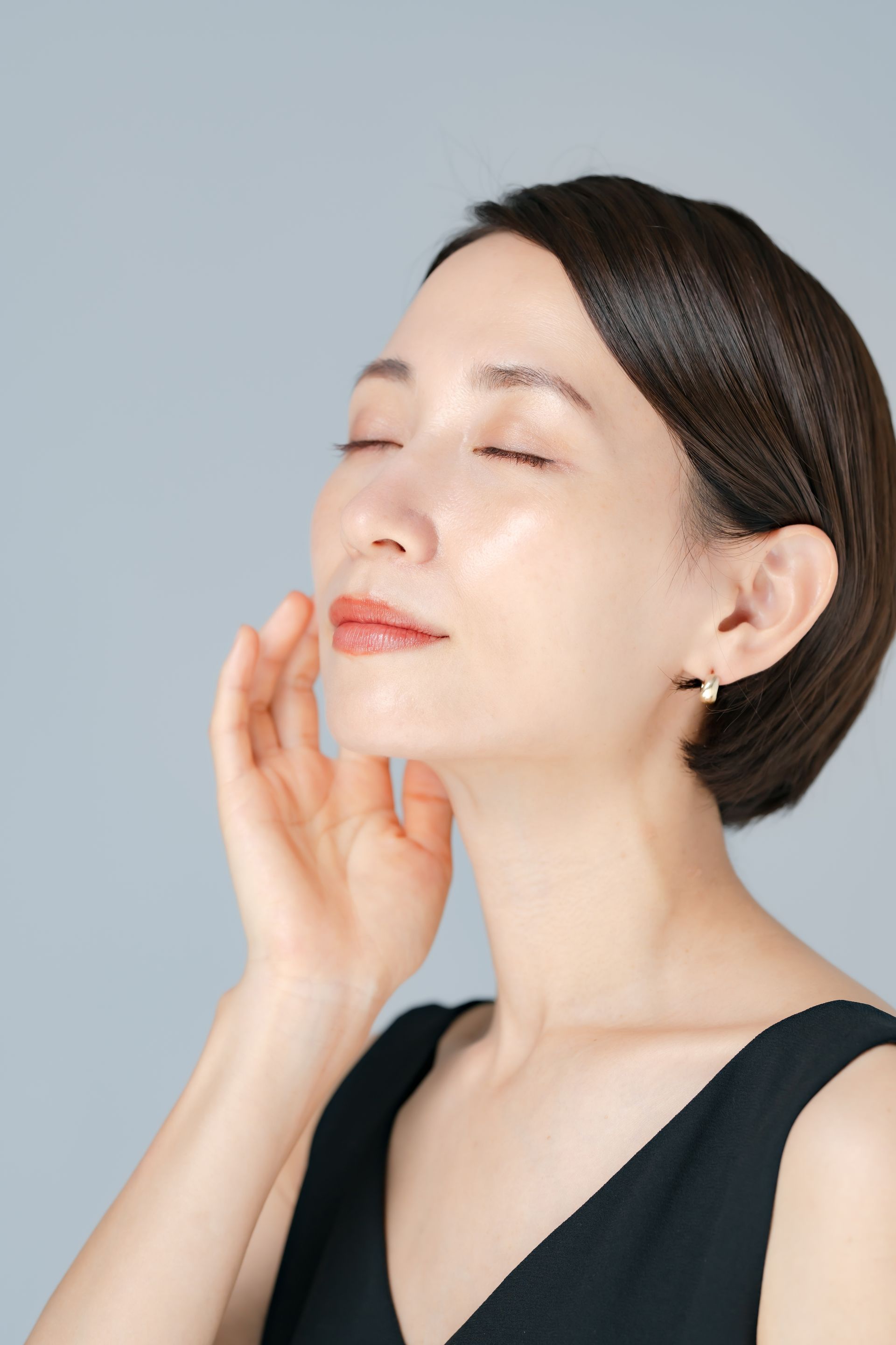 A woman is touching her face with her hand and her eyes closed.
