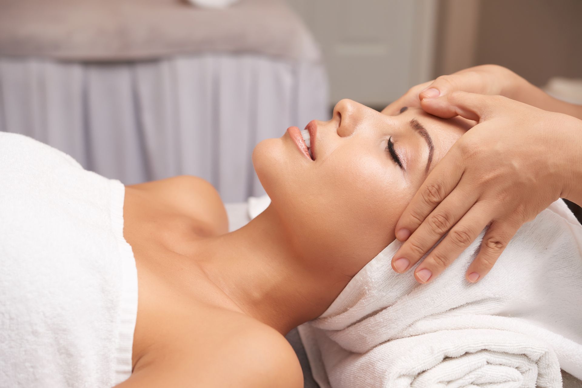 Woman receiving a facial massage at a spa. Hands on forehead, wrapped in a towel.